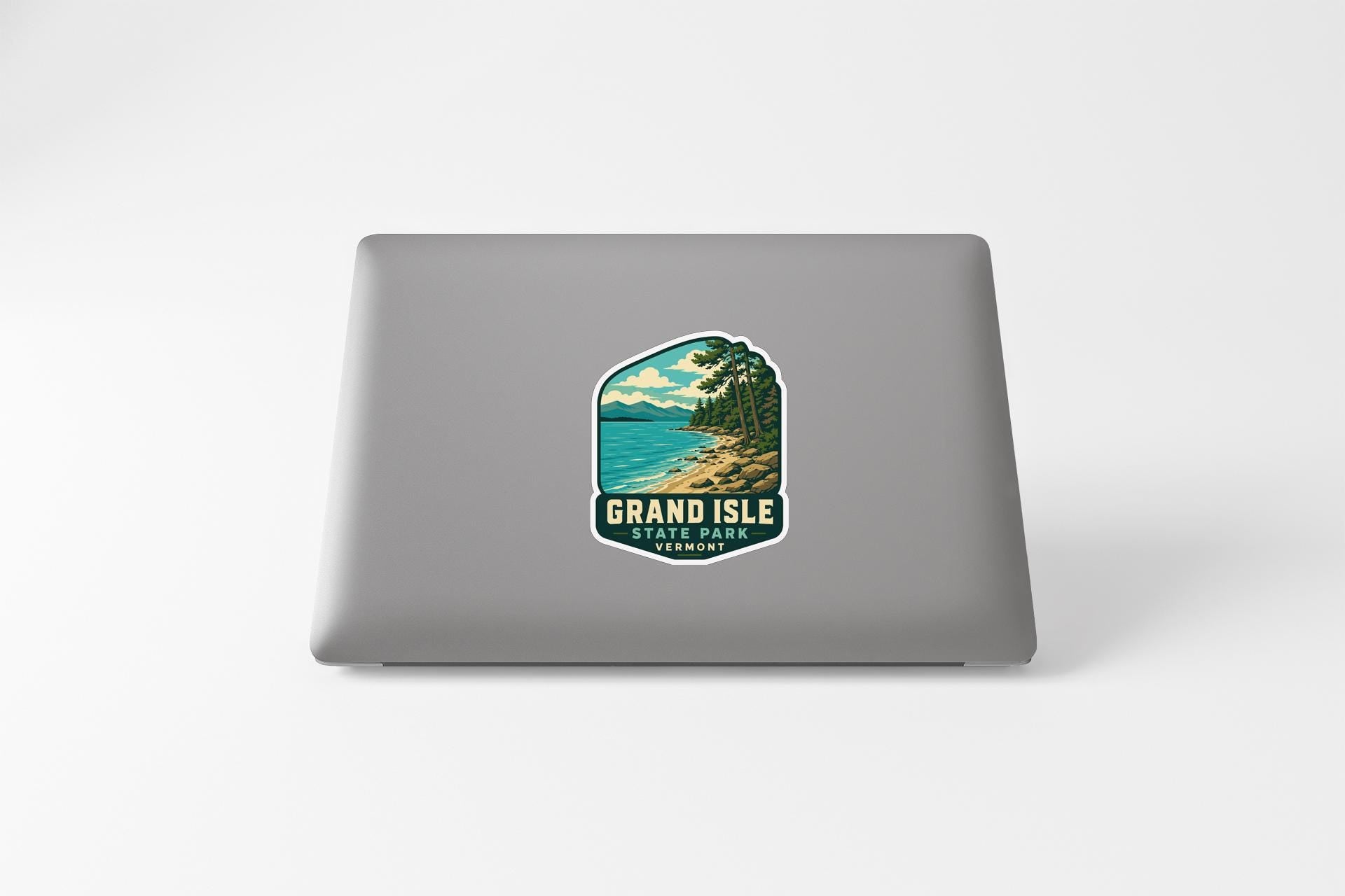 A sticker on the back of a laptop that features a scenic landscape with a lake, mountains, and trees.