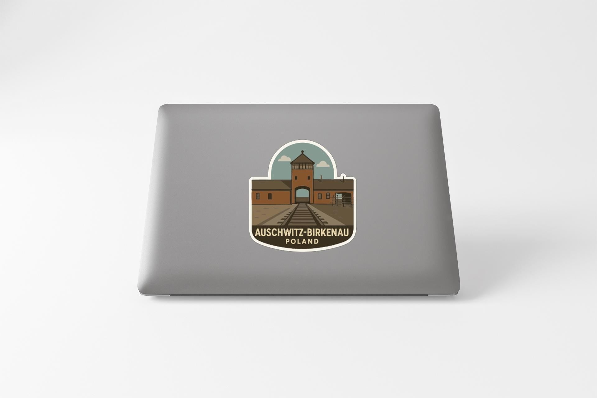 a sticker or decal on the back of a laptop, depicting a building with a tower and the text "AUSCHWITZ-BIKENAU POLAND".