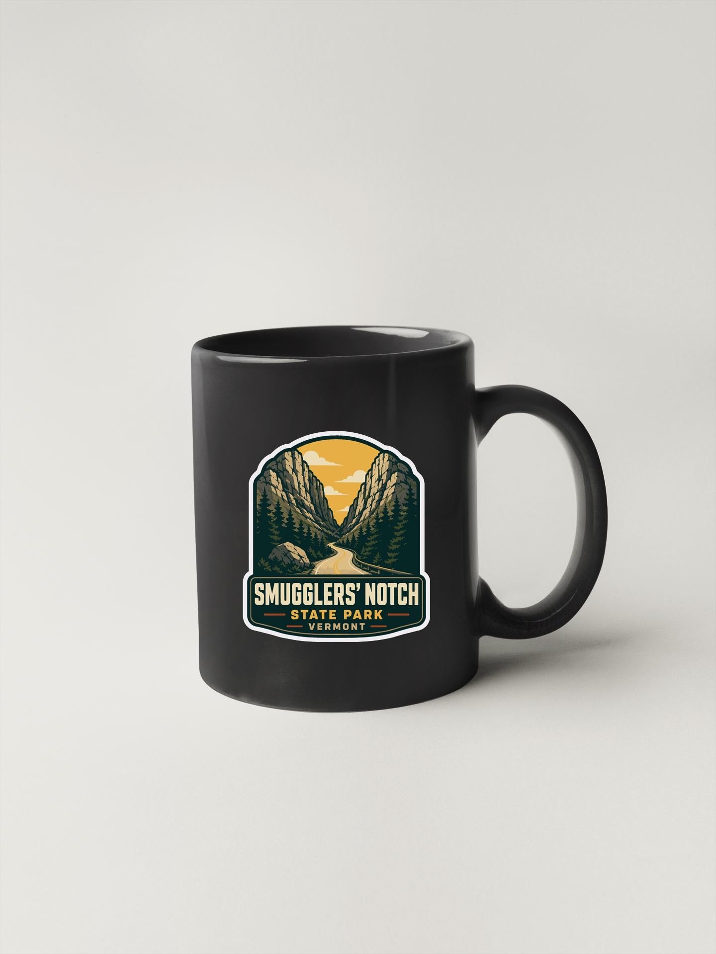 A black coffee mug with a graphic design depicting Smugglers' Notch State Park in the background.