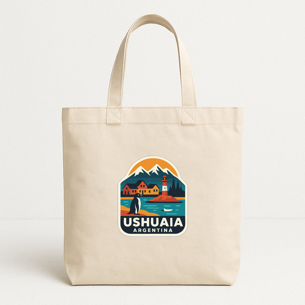 A beige tote bag with a printed design depicting a scenic landscape with mountains, a lighthouse, and a penguin.