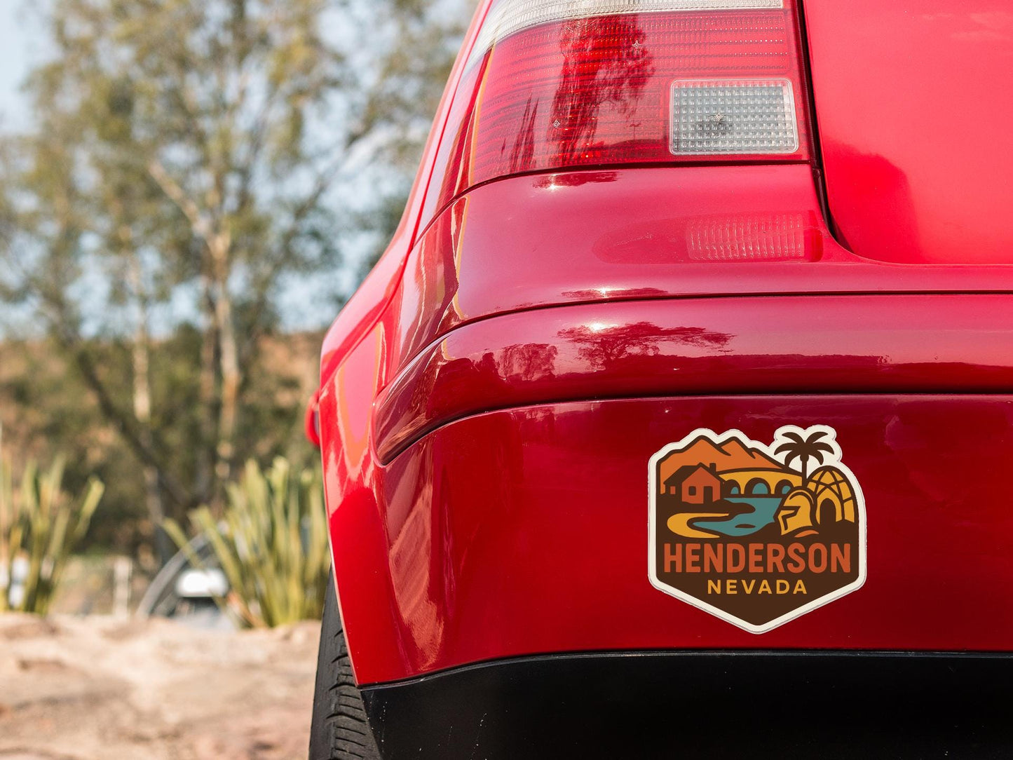 the rear end of a red car with a sticker on the back window that says "Henderson Nevada".