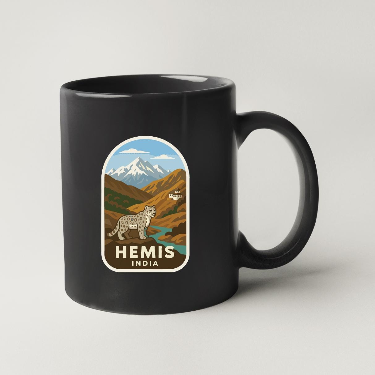 A black coffee mug with a sticker depicting a mountain landscape and a leopard.