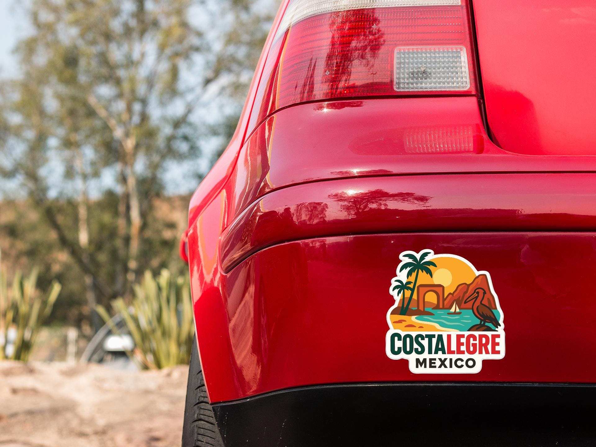 the rear end of a red car with a sticker on it, featuring a tropical beach scene with palm trees and a sunset.