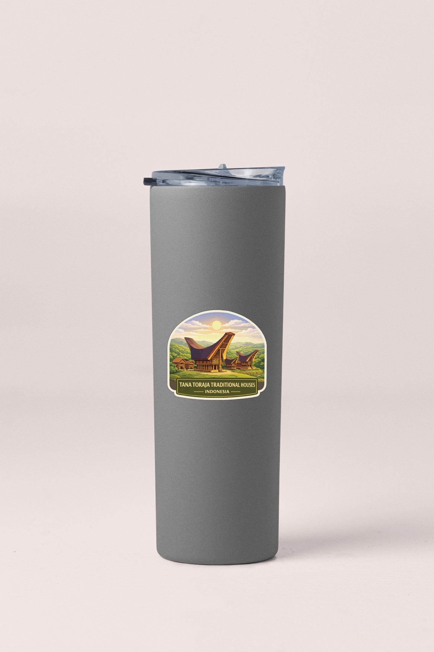 A gray insulated tumbler with a lid and a label featuring an illustration of a dinosaur and the text "Iana Tora Traditional Wike Indonesia".