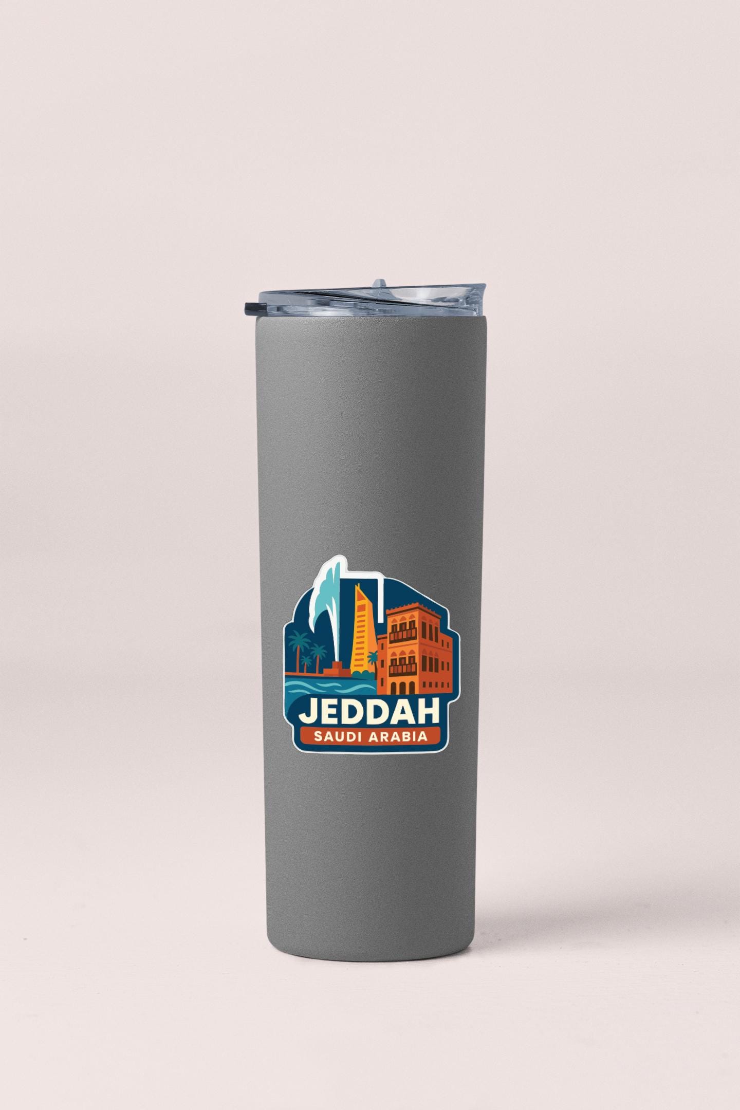 A gray insulated tumbler with a lid and a sticker featuring an illustration of a city skyline and the text "JEDDAH SAUDIABARA".