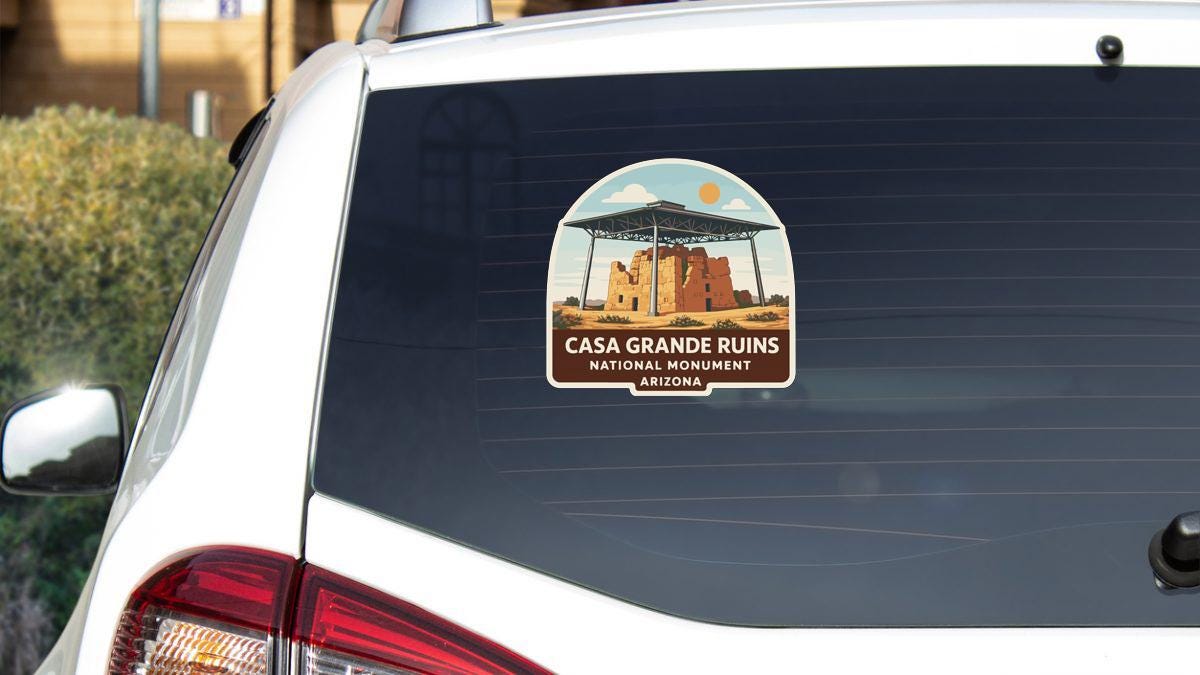 a sticker on the rear window of a white car, depicting the Casa Grande Ruins National Monument in Arizona.