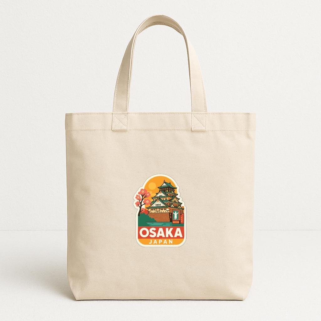 A beige tote bag with a printed design of Osaka, Japan, featuring a castle and a sunset.