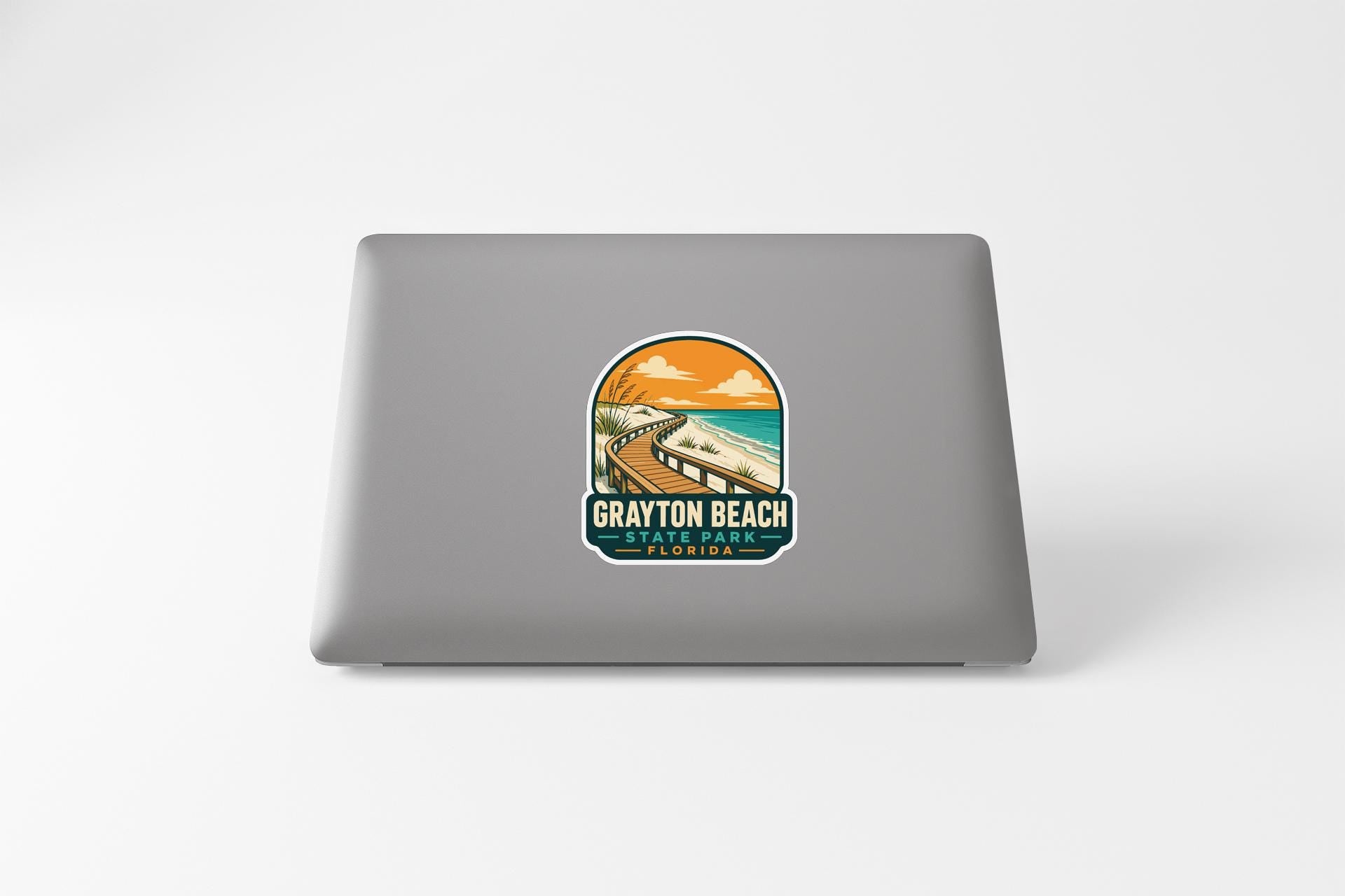 A sticker on the back of a laptop, depicting a scenic beach landscape with a winding road leading to a body of water.