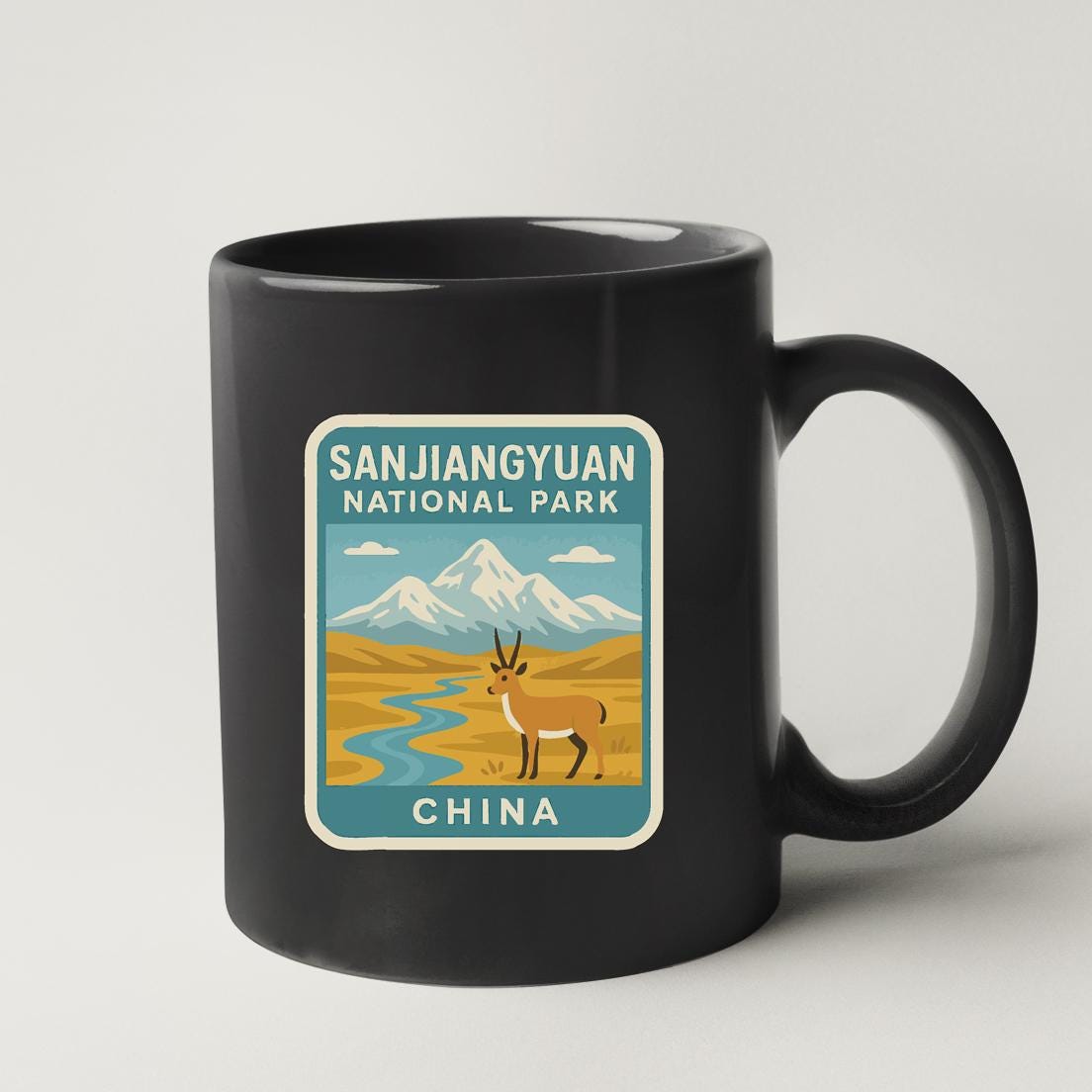 A black coffee mug with a sticker depicting a gazelle in front of a mountain range, along with the text "SANJIANGYUAN NATIONAL PARK CHINA".