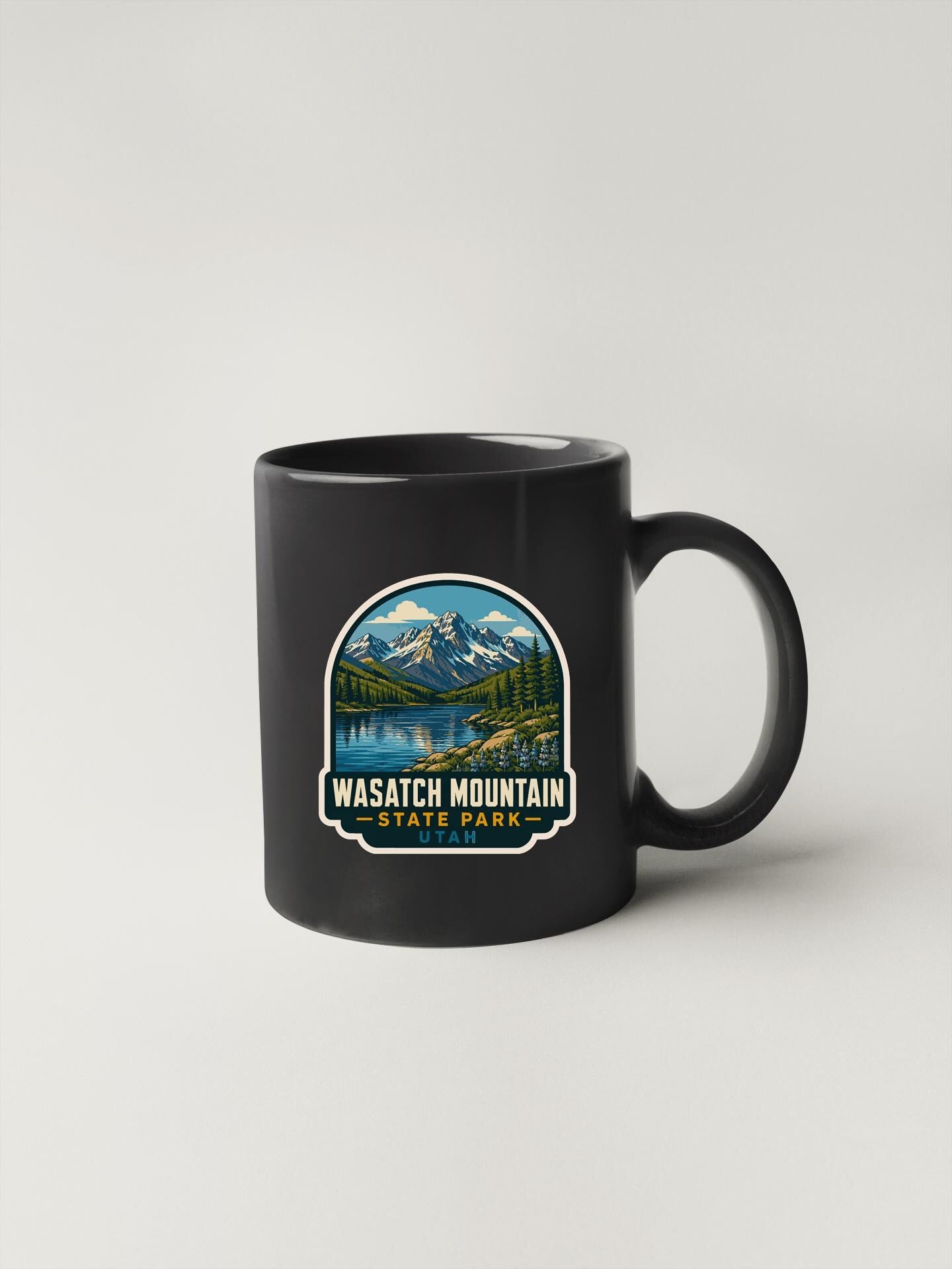 A black coffee mug with a graphic design depicting a scenic mountain landscape and a lake.