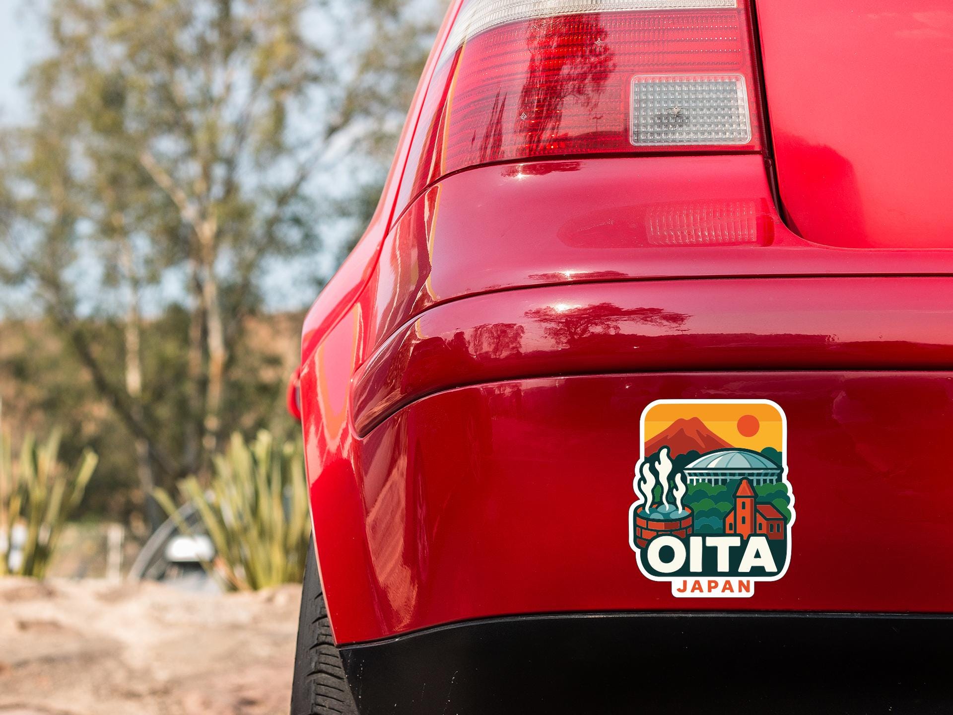 the rear end of a red car with a sticker on the trunk that says "OITA JAPAN".