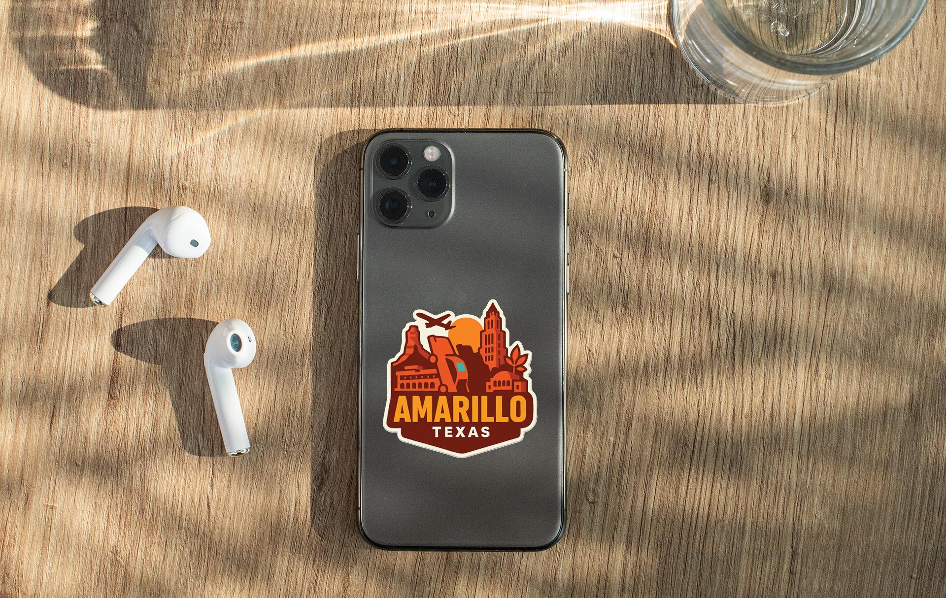 a smartphone with a sticker on the back, placed on a wooden surface alongside a pair of white earbuds and a glass of water.