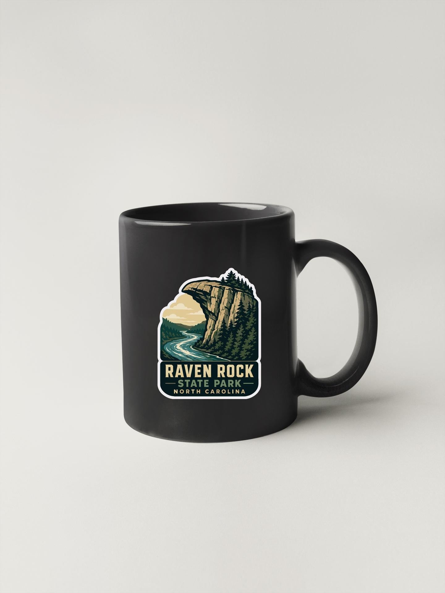 A black coffee mug with a sticker depicting a scenic mountain landscape.