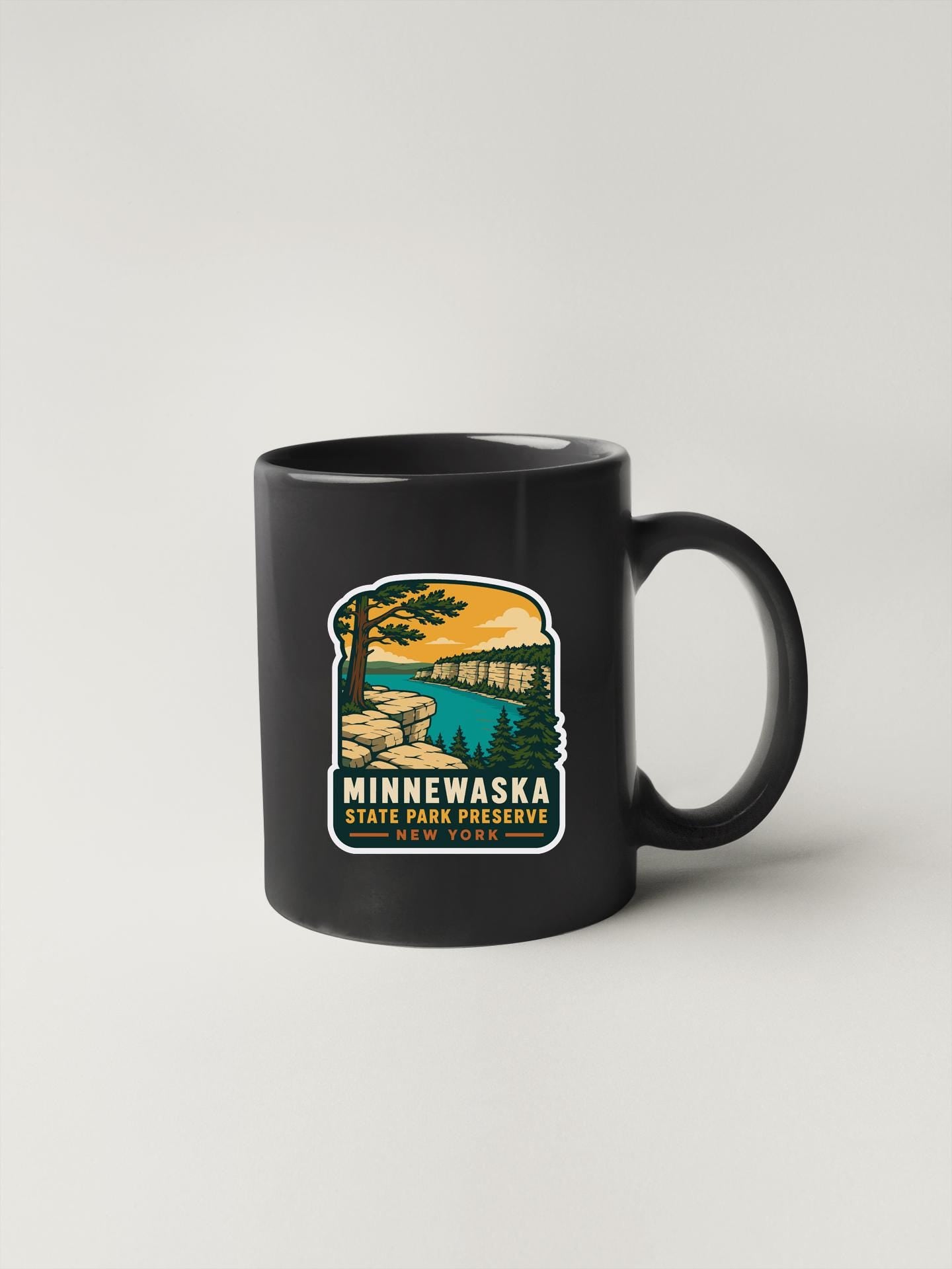 A black coffee mug with a graphic design depicting a scenic landscape, including a lake, mountains, and trees.