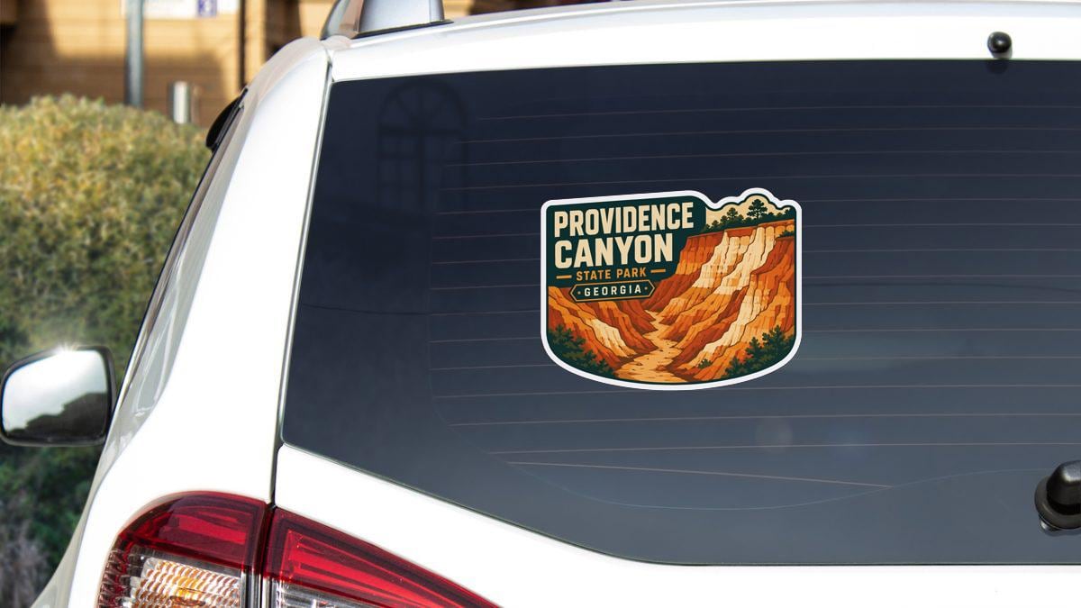 A sticker on the rear window of a white car, depicting the scenic landscape of Providence Canyon, a state park in Georgia.