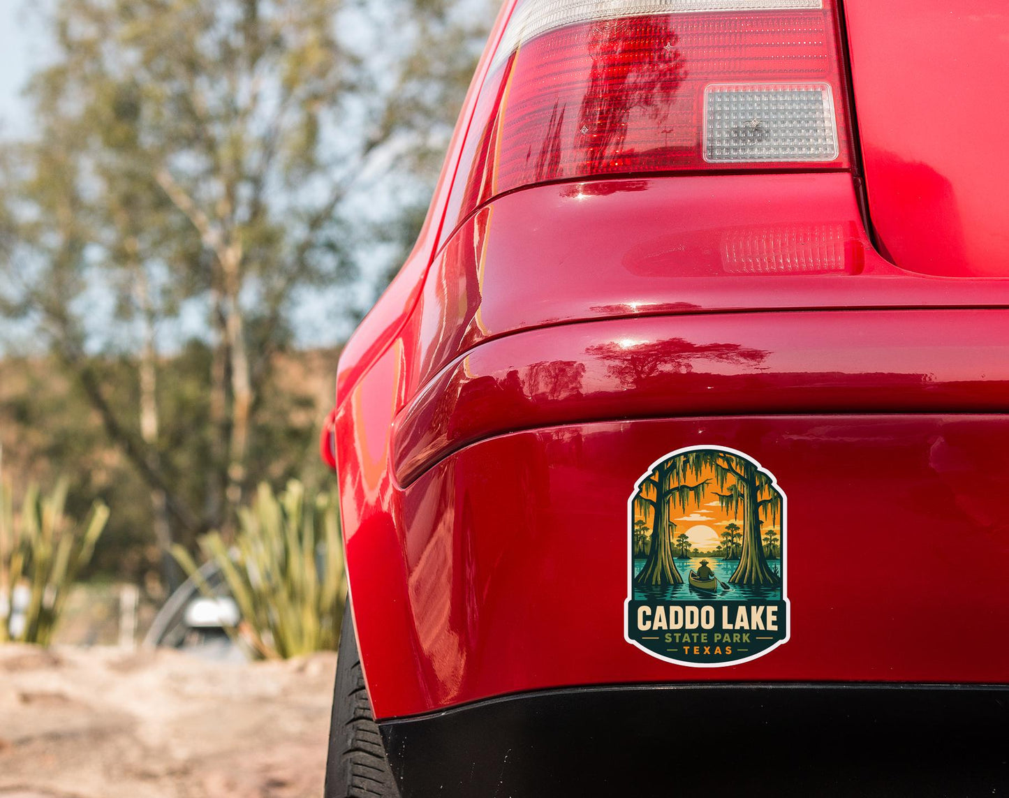 the rear end of a red car with a sticker on the trunk that says "CADDO LAKE CADDO PARK TEXAS".