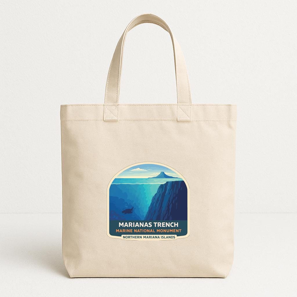 A beige tote bag with a graphic design featuring a mountain landscape and the text "Marianas Trench" and "Northern Mariana Islands".