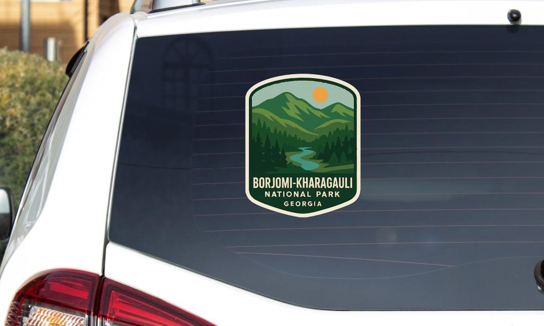 A sticker on the rear window of a car, depicting a scenic mountain landscape with a river and sun.