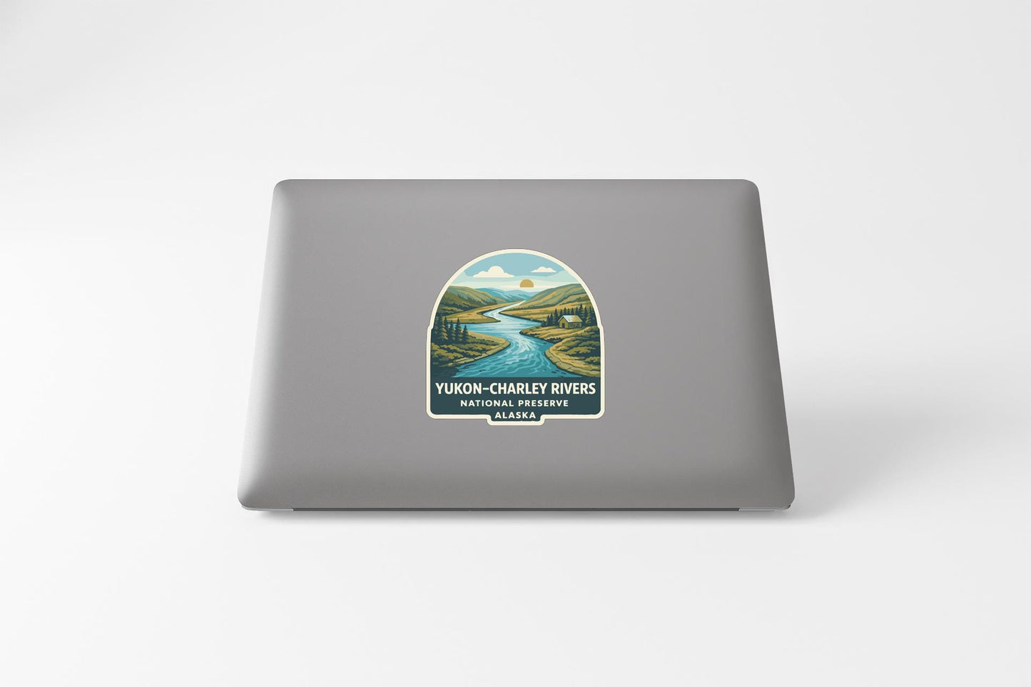 a sticker on the back of a laptop that depicts a scenic landscape with a river and mountains.