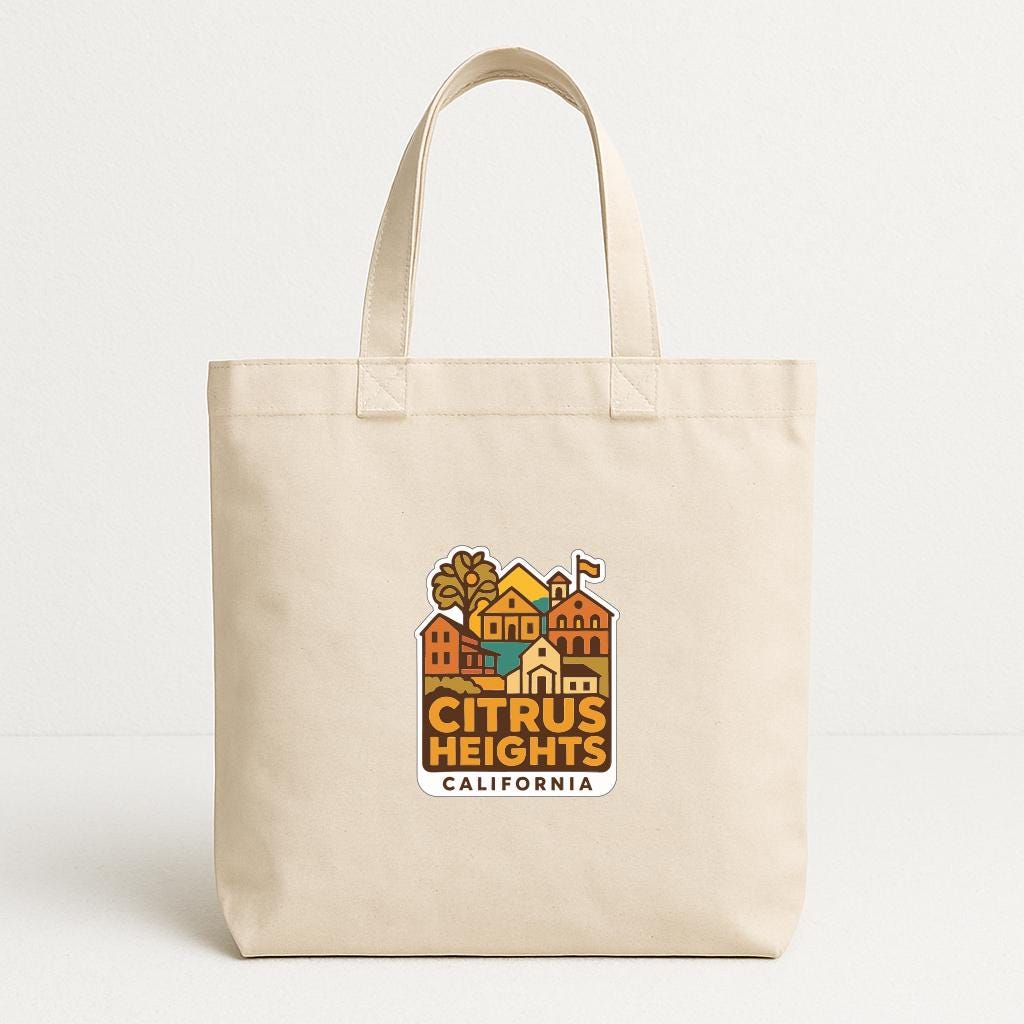 A beige tote bag with a graphic design featuring a colorful illustration of a cityscape and the text "CITRUS HEIGHTS, CALIFORNIA".