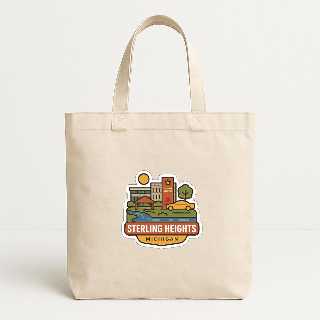 A beige tote bag with a printed design depicting a cityscape and the text "STERLING HEIGHTS MICHIGAN" printed on it.