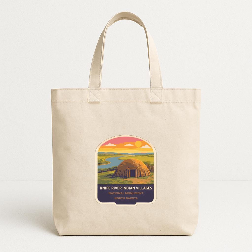 A beige tote bag with a graphic design depicting a Native American village at sunset.
