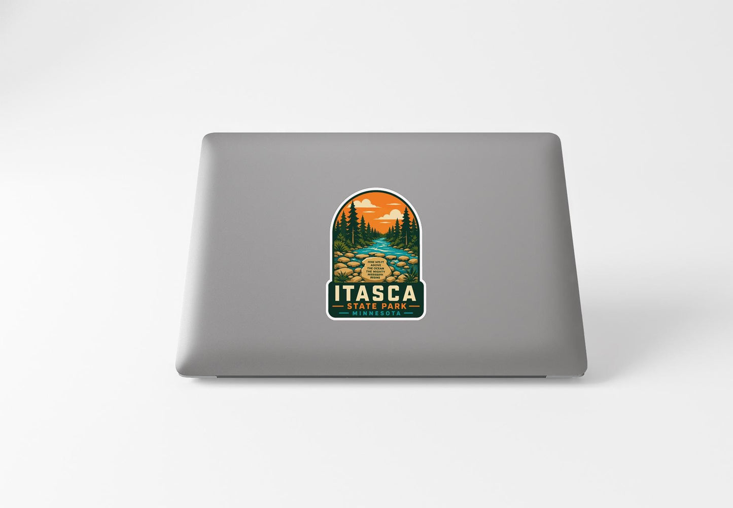 A sticker on the back of a laptop, depicting a scenic landscape with a river, trees, and mountains.