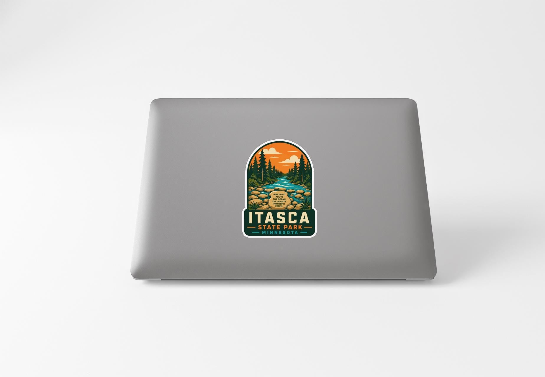 A sticker on the back of a laptop, depicting a scenic landscape with a river, trees, and mountains.
