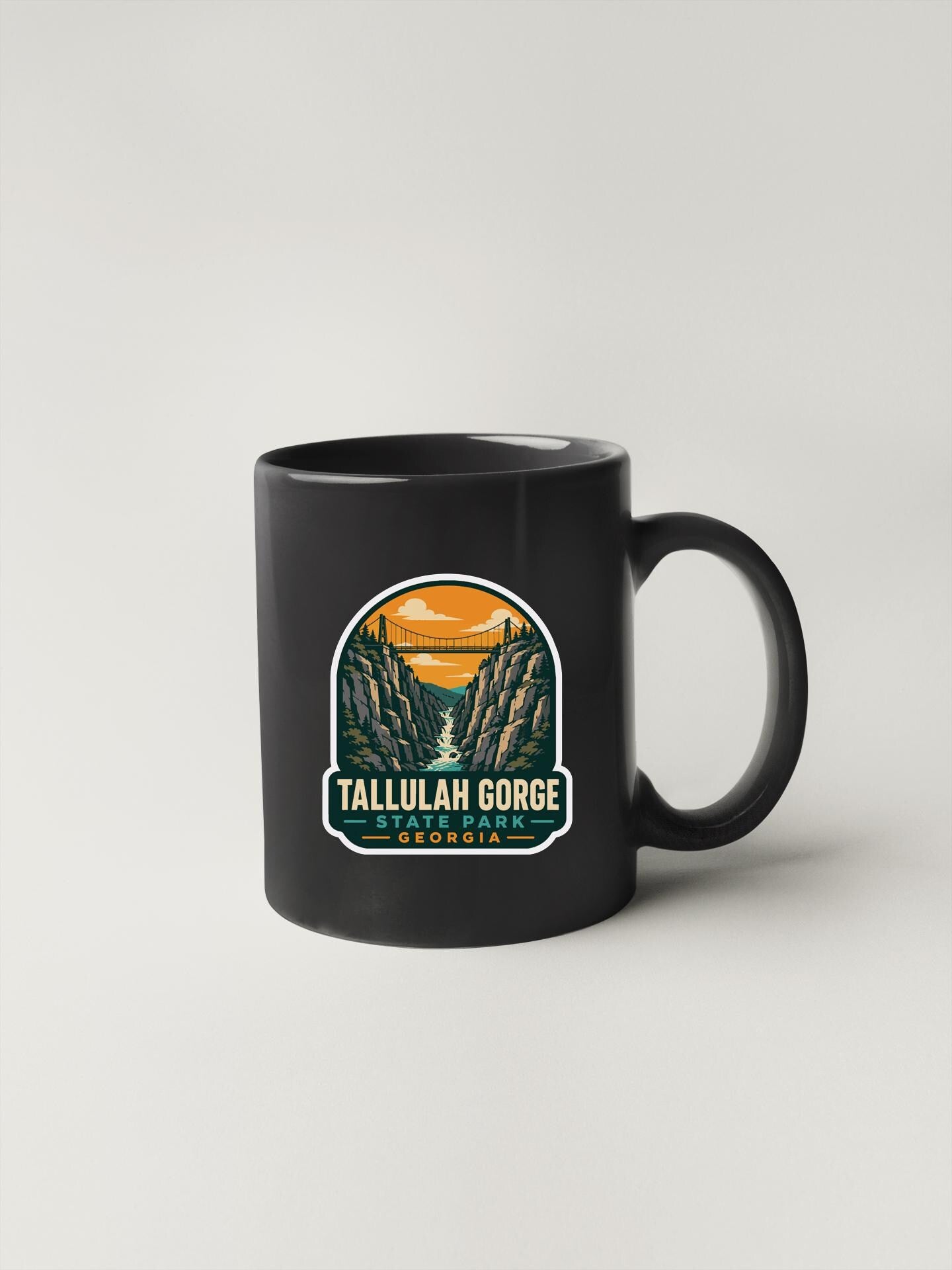 A black coffee mug with a graphic design depicting Tallulah Gorge, a scenic mountain range in Georgia.