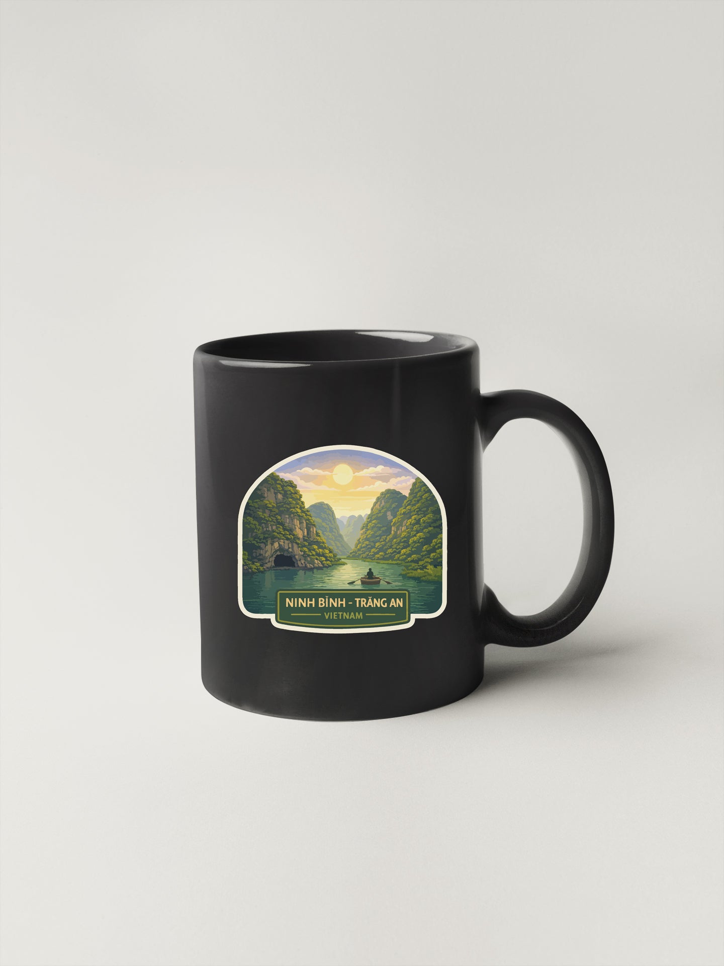 A black coffee mug with a sticker depicting a scenic landscape, including mountains, a river, and a sunset.