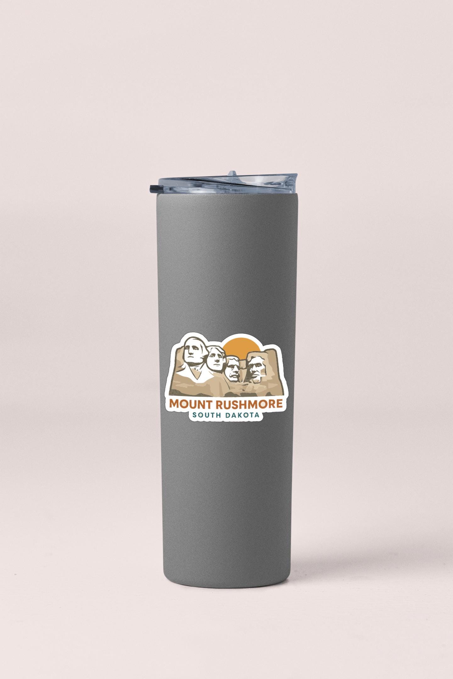 A gray insulated tumbler with a printed logo featuring the Mount Rushmore monument in South Dakota.