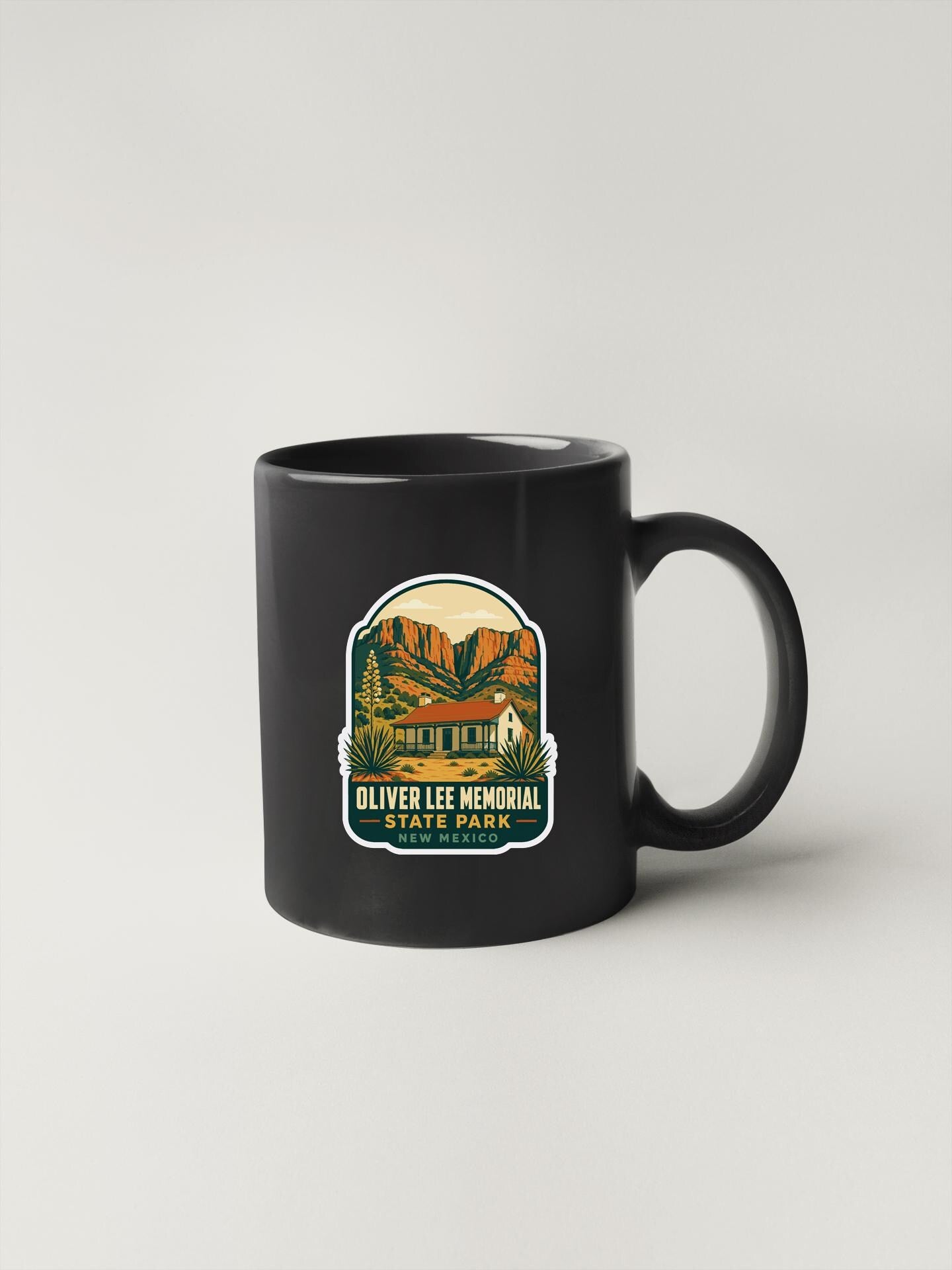 A black coffee mug with a graphic design depicting a scenic landscape, including mountains, trees, and a building, along with the text "OLIVER LEE MEMORIAL STATE PARK NEW ORLEANS".