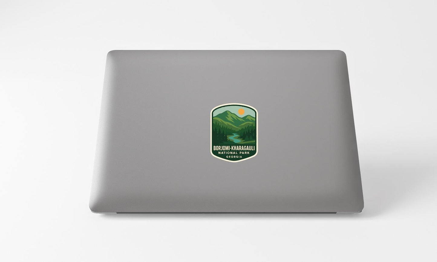 A sticker on the back of a laptop, depicting a mountain landscape with a river and sun.