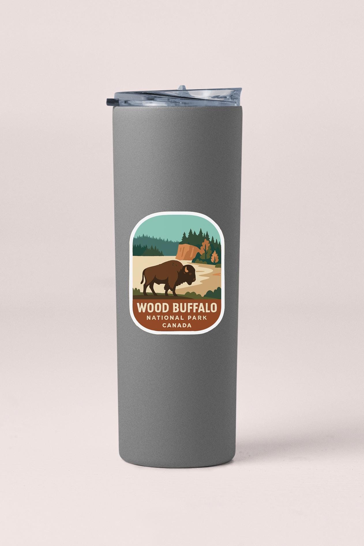 A gray insulated tumbler with a label that features an illustration of a bison in a forest setting, along with the text "WOOD BISON NATIONAL PARK CANADA".