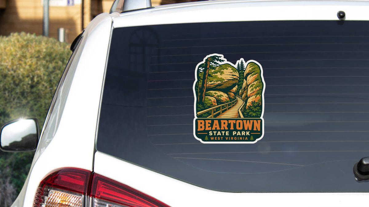 A sticker on the rear window of a white car, depicting a scenic landscape with a path leading to a mountain.