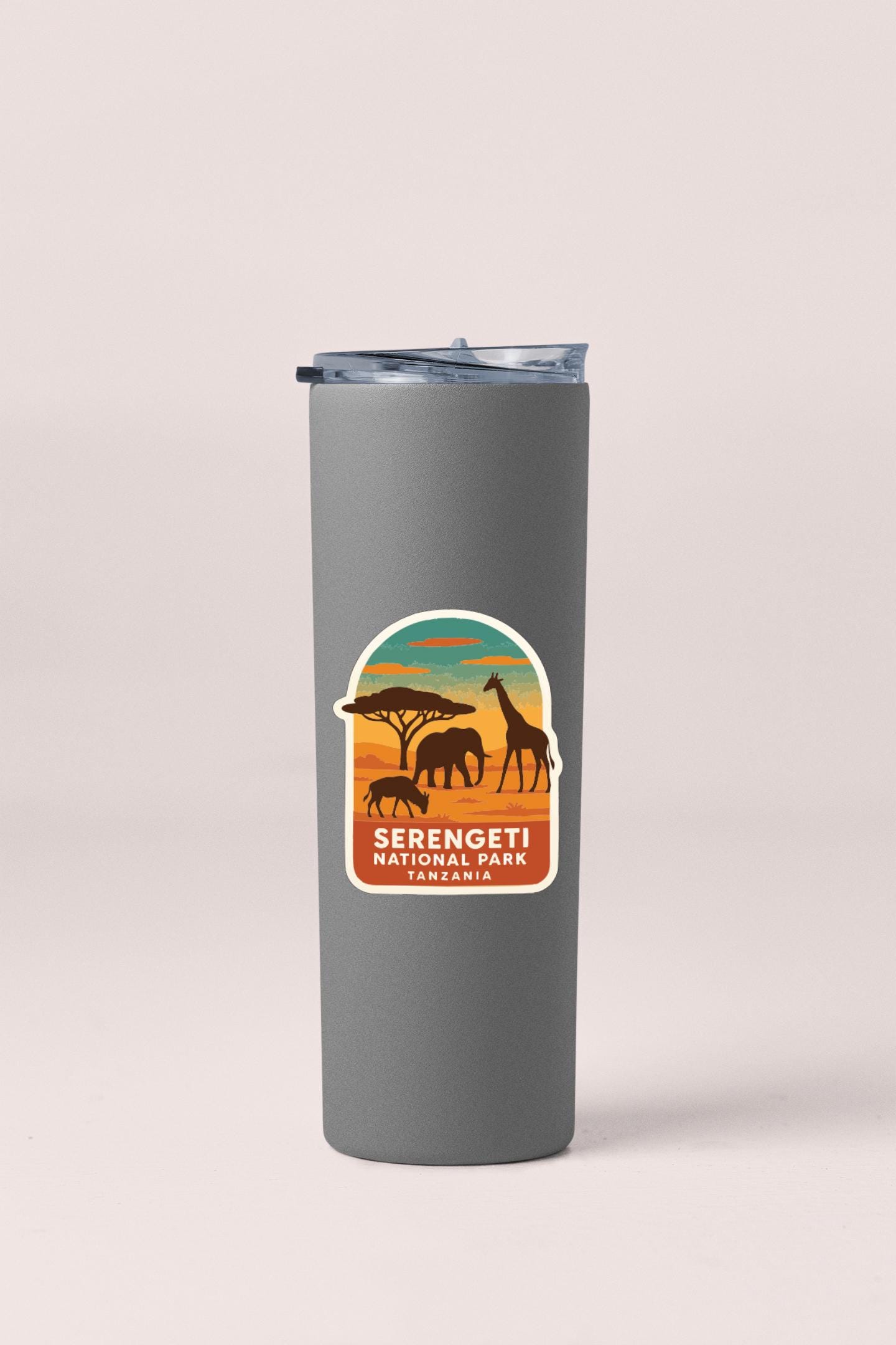 A gray insulated tumbler with a label that features an illustration of wildlife, including elephants, giraffes, and a tree, along with the text "Serengeti National Park Tanzania".