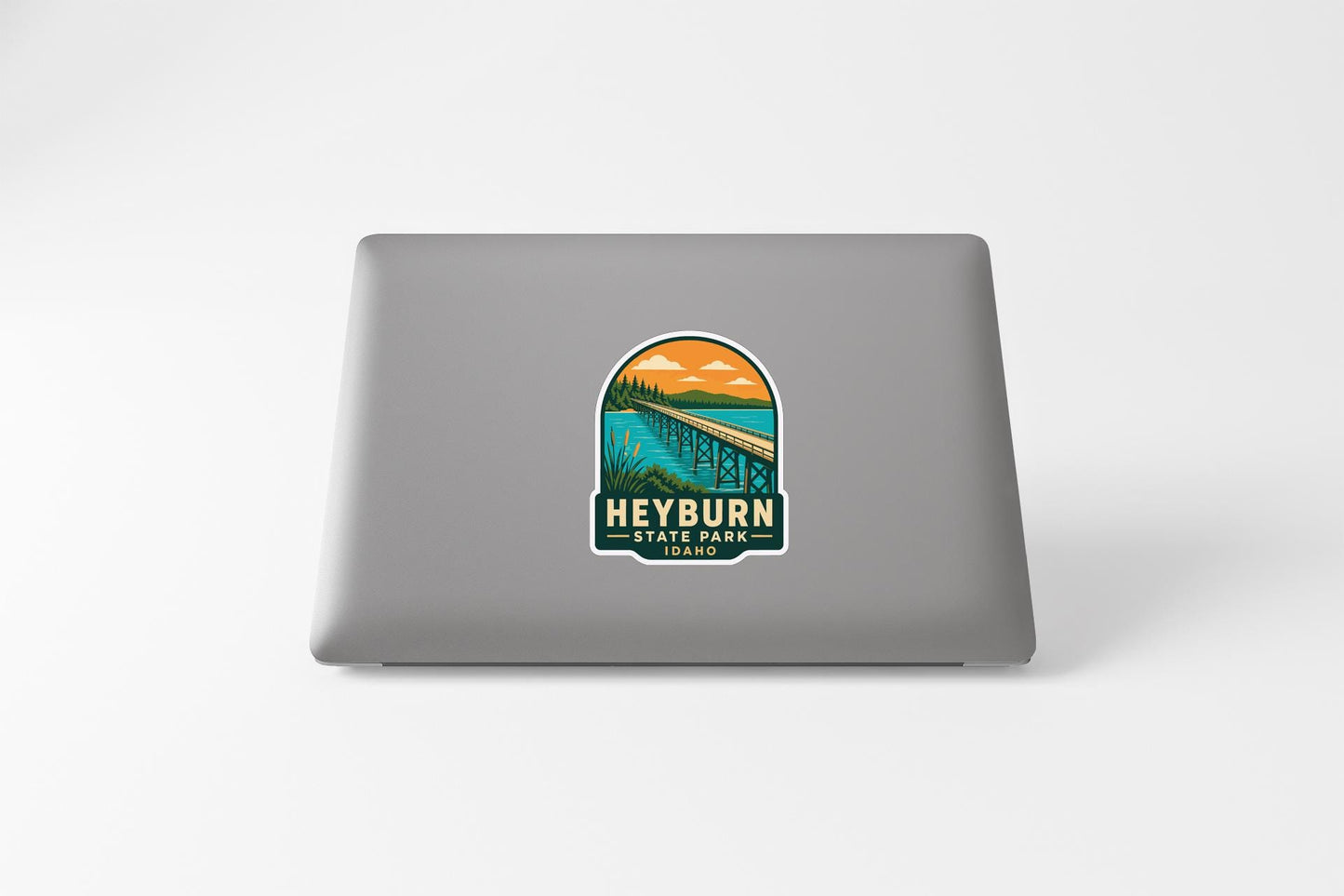 a sticker on the back of a laptop that displays a scenic landscape with a bridge and a body of water.