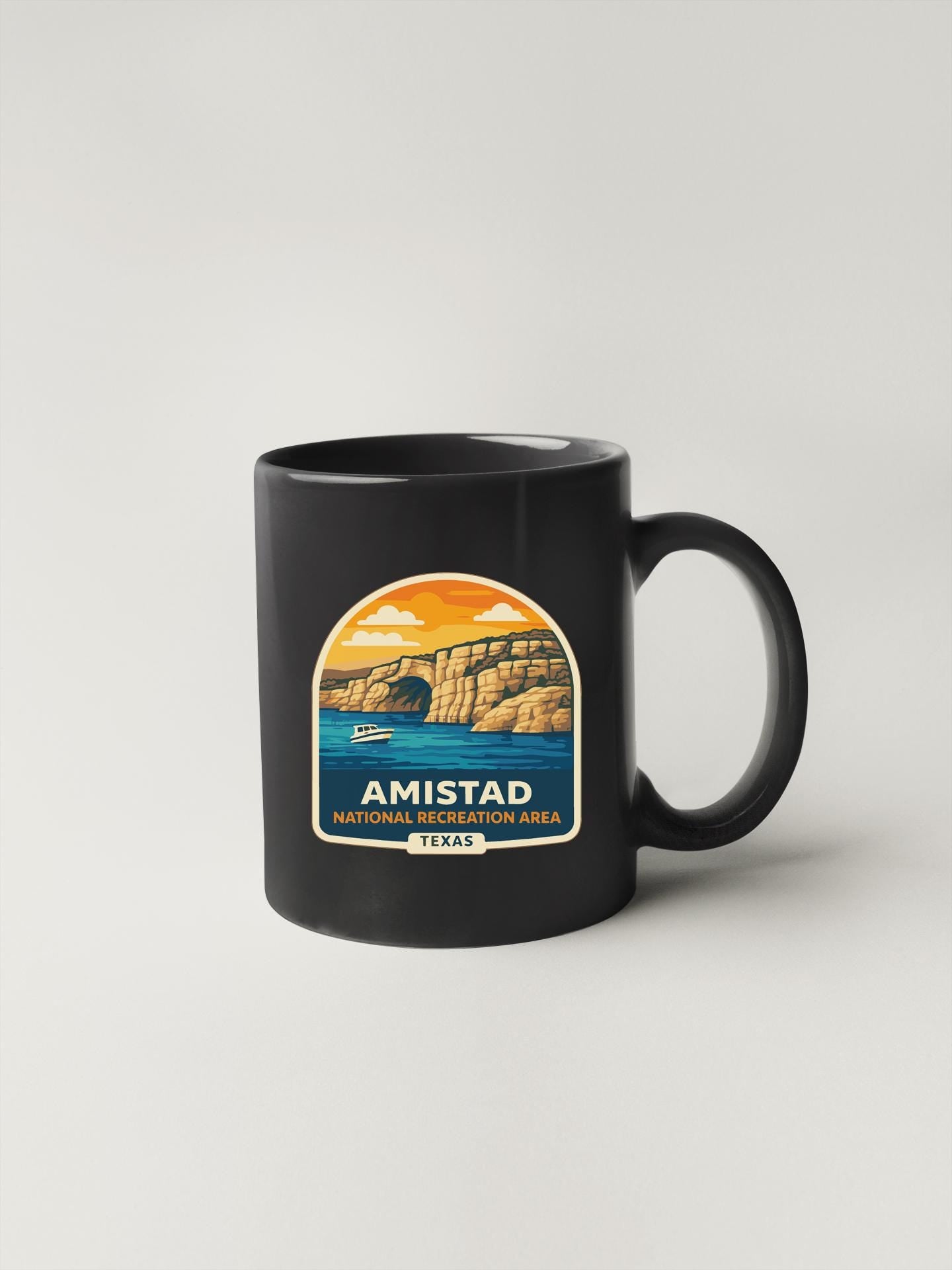 A black coffee mug with a graphic design depicting a scenic landscape, including a cliff, water, and a boat.