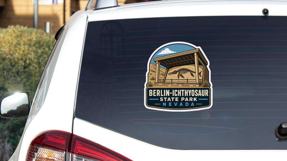 a sticker on the rear window of a white car, depicting a scenic view of Berlin-Ichthyosaur State Park, Nevada.