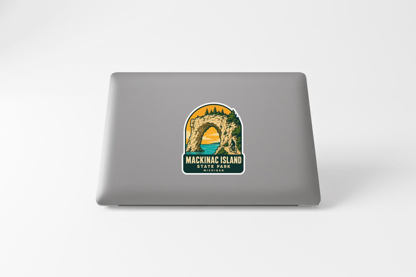 A sticker on the back of a laptop, depicting a scenic landscape with a bridge and trees, representing Mackinac Island State Park.