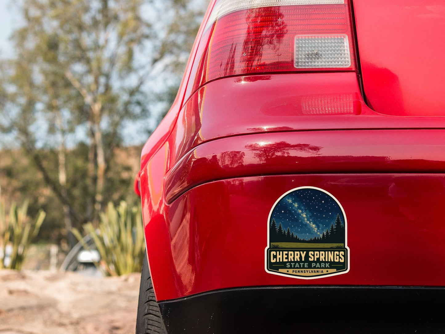 the rear end of a red car with a sticker on the back window that reads "CHERRY SPRINGS STATE PARK PENNSYLVANIA".