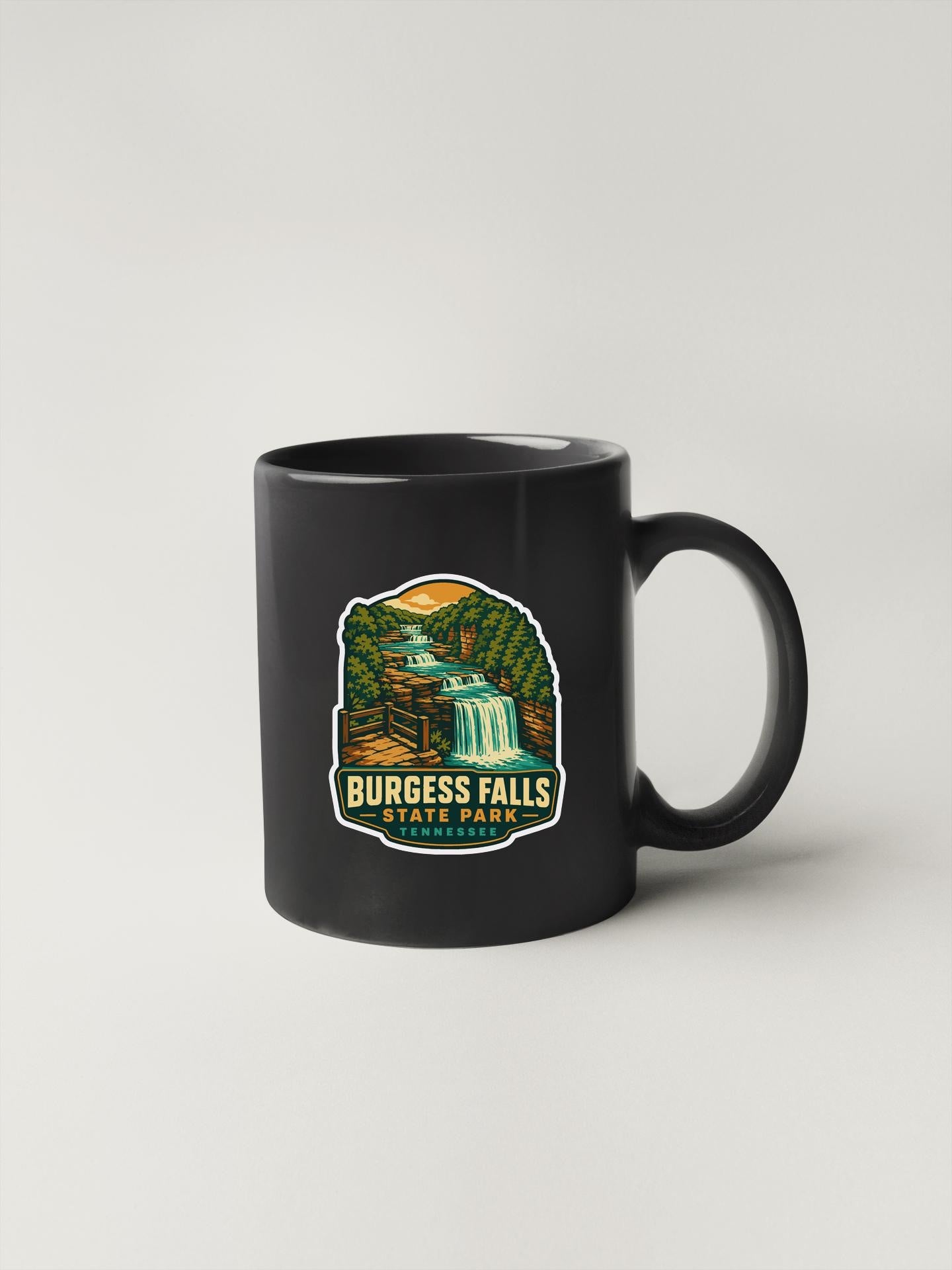 A black coffee mug with a graphic design depicting a waterfall and forest.