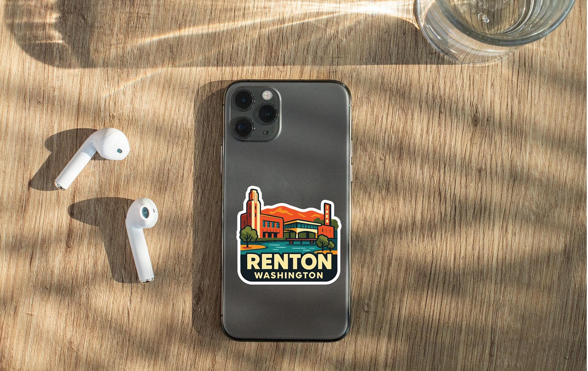 a smartphone with a sticker on the back, placed on a wooden surface alongside a pair of white earbuds and a glass of water.