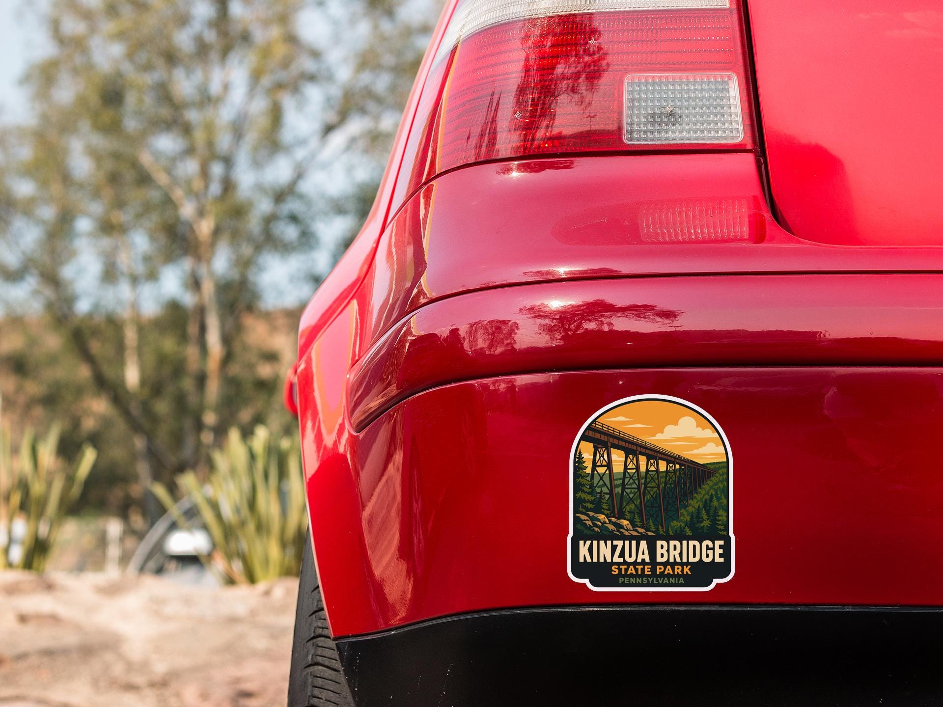 the rear end of a red car with a sticker on the back window that reads "KINZIA BRIDGE STATE PARK".