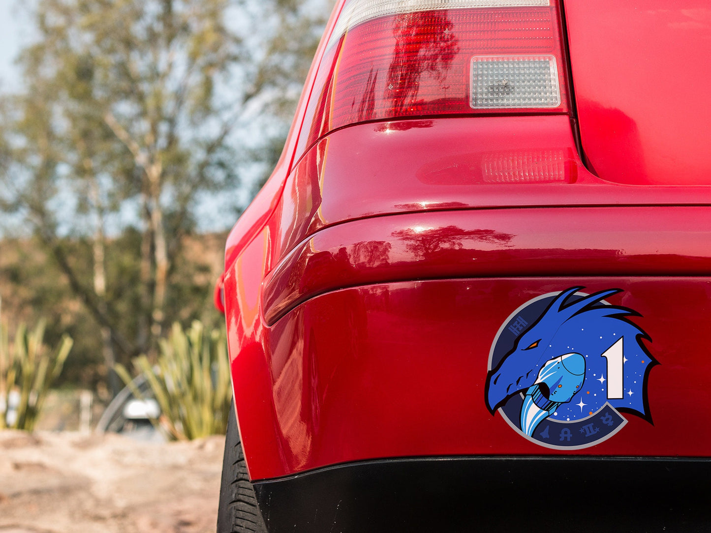 the tail end of a red car with a blue bear sticker on it