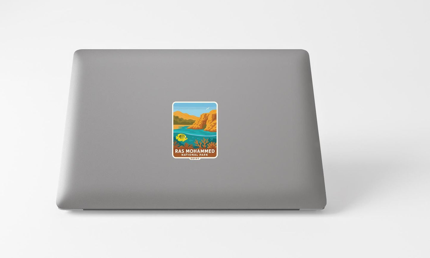 A sticker on the back of a laptop, depicting a scenic landscape with mountains, water, and a clear blue sky.