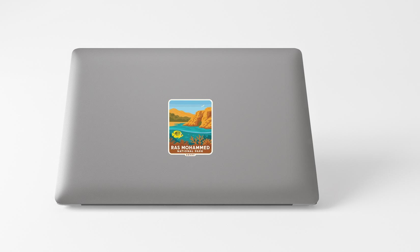 A sticker on the back of a laptop, depicting a scenic landscape with mountains, water, and a clear blue sky.