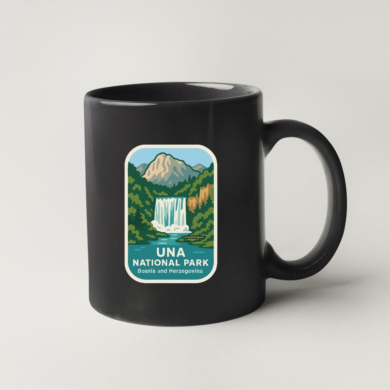 A black coffee mug with a label that features a scenic image of a waterfall and mountains, along with the text "UNA NATIONAL PARK BOSNIA and HERZEGOVINA".