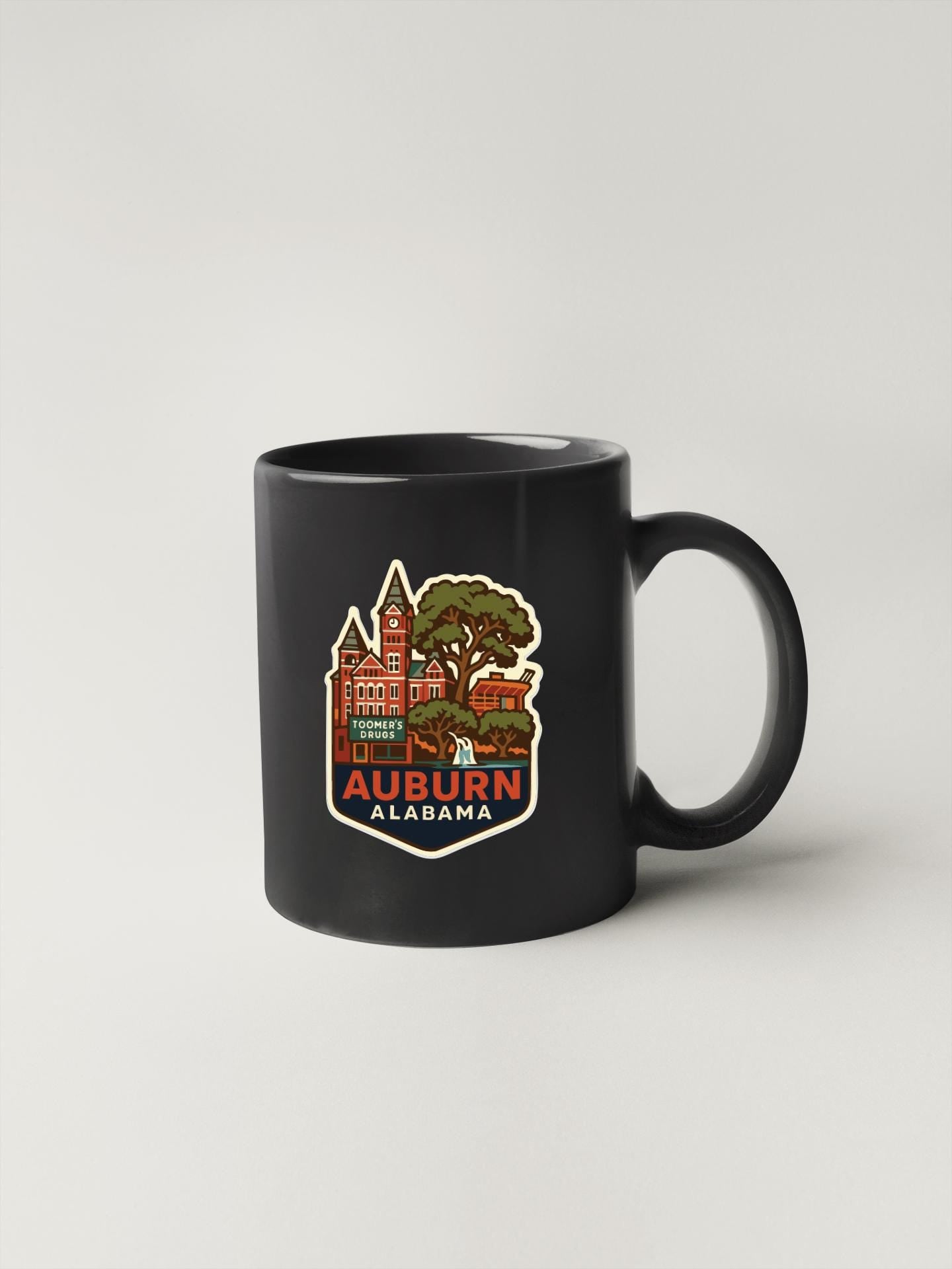 A black coffee mug with a graphic design depicting a building and trees, along with the text "AUBURN ALABAMA" printed on it.