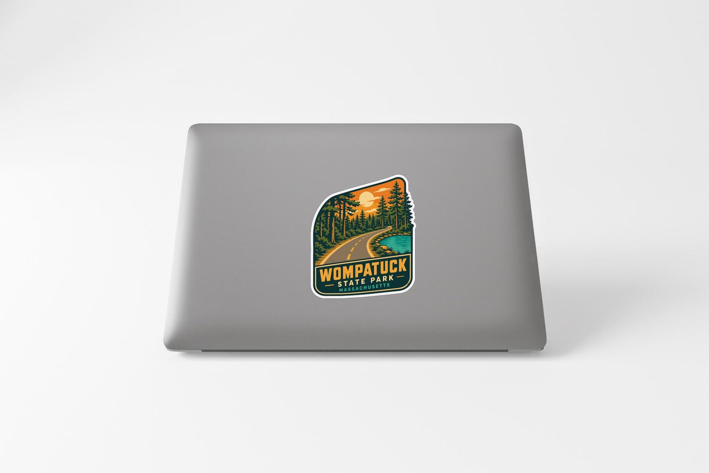 A sticker on the back of a laptop, depicting a scenic road leading through a forested area with a sunset in the background.